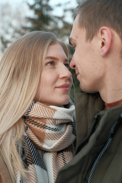 A woman with blonde hair looking gently at her boyfriend in a winter forest