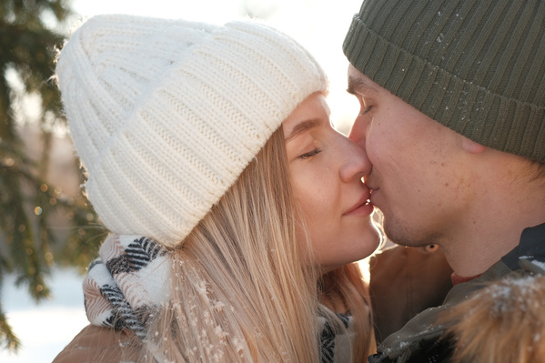 A guy and his beloved in warm clothes kissing in the snowy forest