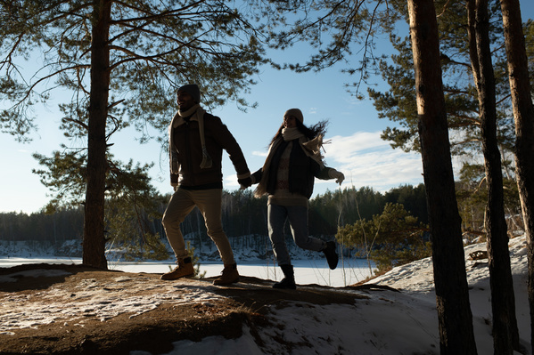 A romantic couple in warm clothes running on the snow-covered rocks with larches