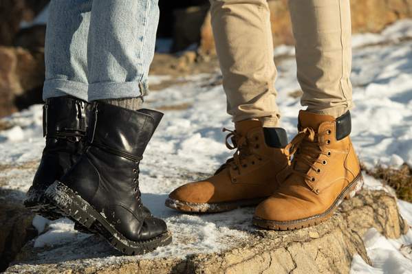 Close-up of the feet of a romantic couple dressed in warm clothes on a walk on snow-covered rocks