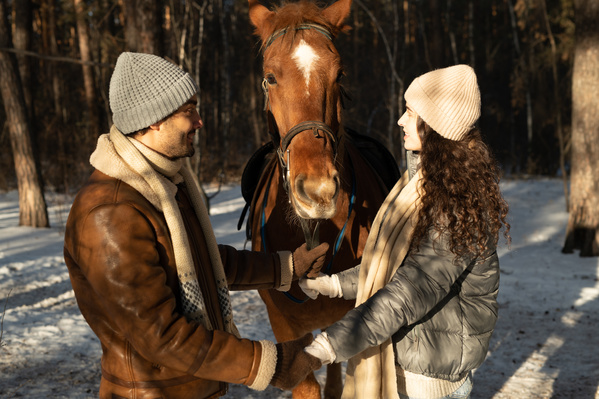 A romantic couple dressed warmly with joined hands on a horse ride in the winter forest