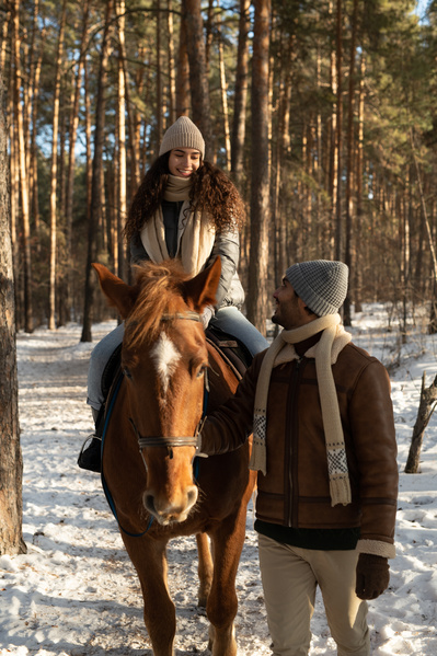 A man helping his dark-haired beloved to ride a horse in the winter forest