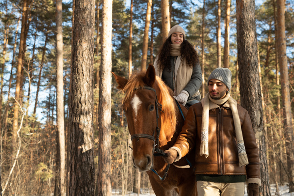 A man helping his dark-haired girlfriend to ride a stallion in the winter forest