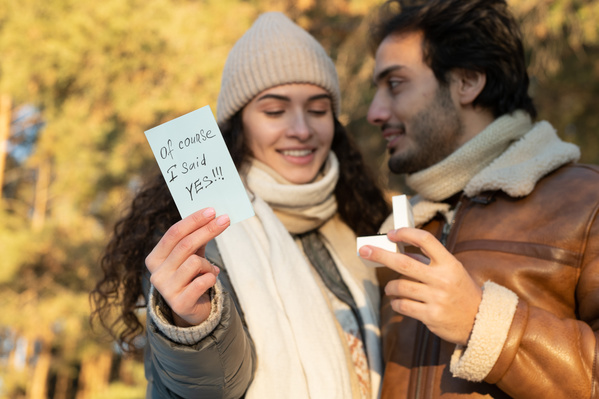 A man in a sheepskin coat proposing to his girlfriend holding a romantic note in her hand outdoor