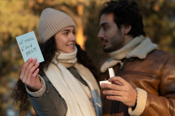 A man in a sheepskin coat proposing to his beloved holding a romantic note in her hand outdoor
