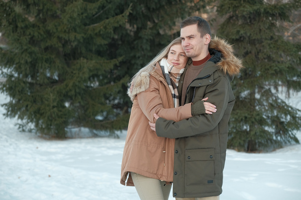A couple in love wearing warm clothes walikng in the winter forest