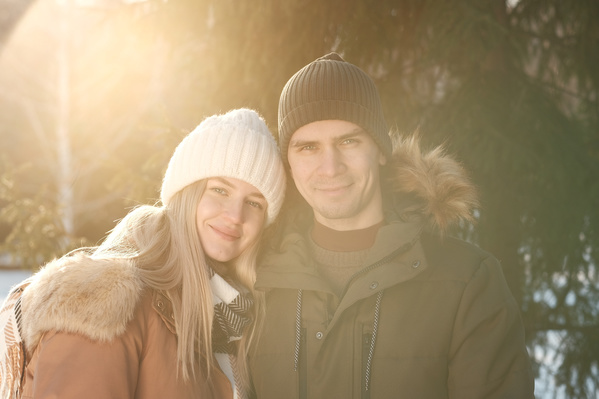 A man and a woman in a winter forest full of the light of sun rays