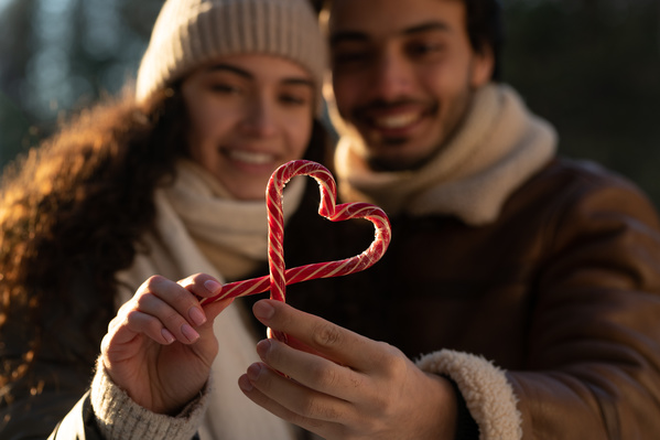 A man and a woman in warm clothes holding lollipops in the shape of a heart
