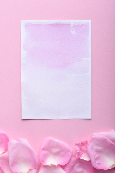 A purple romantic greeting card and pink petals on a pink surface
