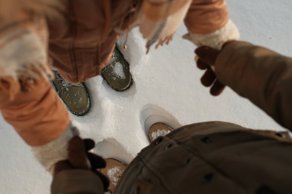 A couple in light winter boots standing in the fresh snow and joining hands