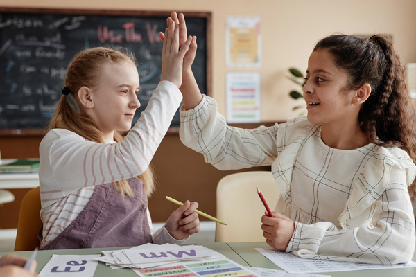 The Image Two Girls Are High Fiving Each Other in a Classroom