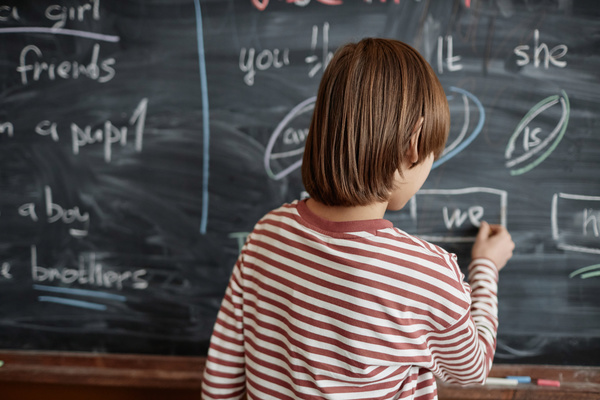 In the image a young girl wearing a striped shirt is standing in front of a chalkboard.