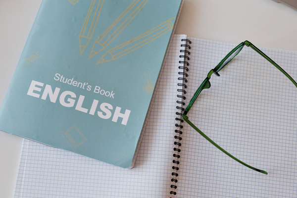 The image features a notebook with the title student's book english and a pair of eyeglasses resting on top of it.