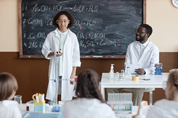 Two People in Lab Coats Standing in Front of a Chalkboard