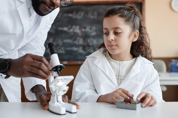 A Man in a Lab Coat Helping a Young Girl with a Microscope