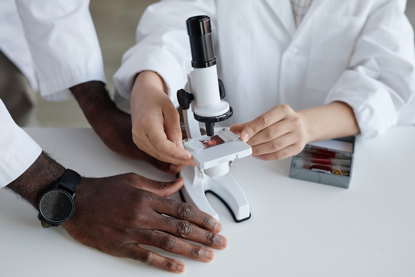 In this image two people are examining an object through a microscope.