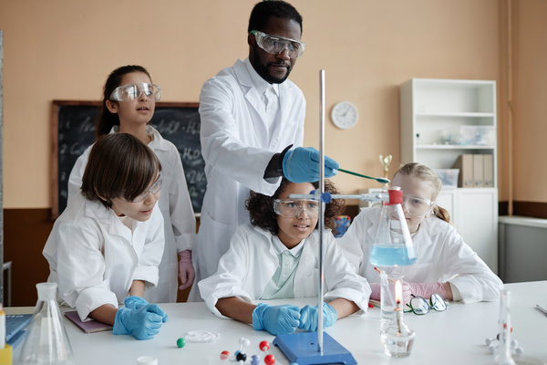 In this image a group of children and an adult are engaged in a science experiment in a classroom setting.