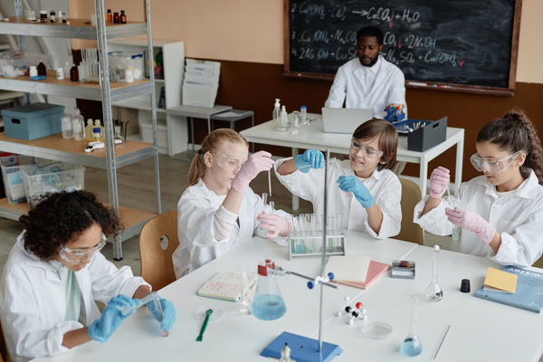 In this image a group of young children are gathered around a table in a laboratory setting.