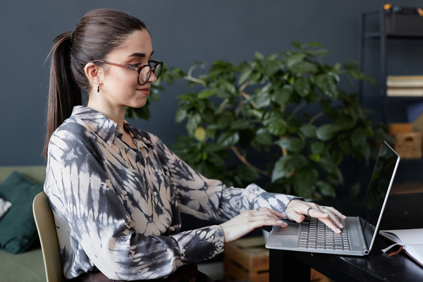 A Woman Wearing Glasses Sitting at a Desk Using a Laptop