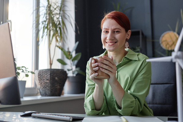 A Smiling Woman Sitting at a Desk with a Cup of Coffee