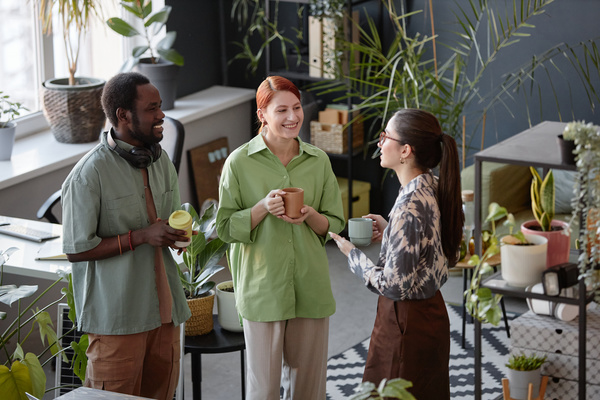 Three People Standing in an Office with Potted Plants and Coffee Cups