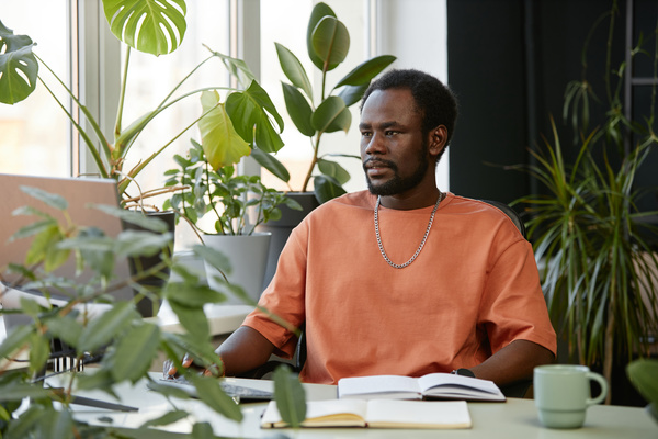 A Man in an Orange Shirt Sitting at a Desk with Plants