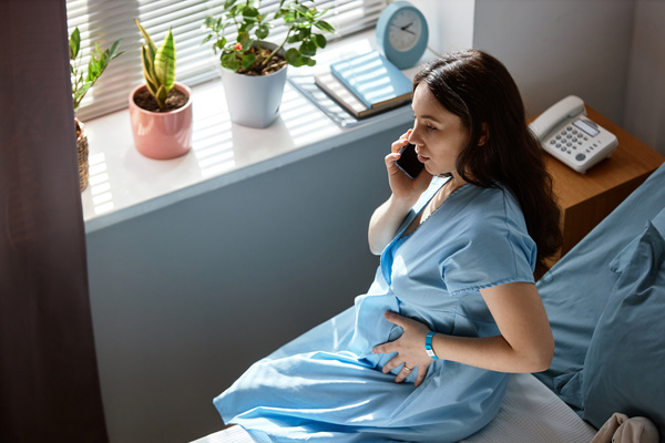 In this image a pregnant woman is sitting on a bed while talking on a cell phone.