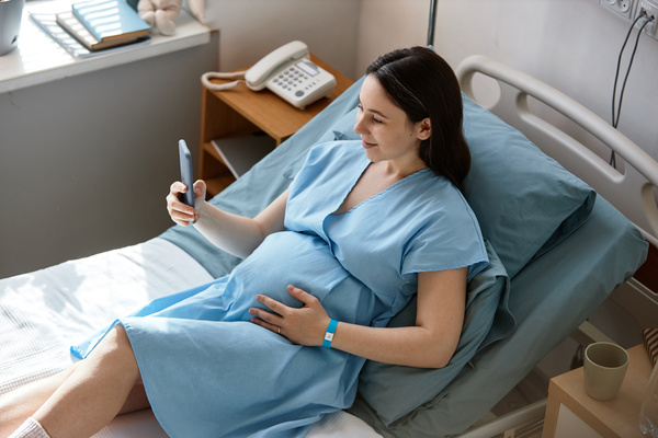 A Pregnant Woman Sitting in a Hospital Bed Holding a Cell Phone