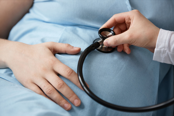 In this image a pregnant woman is being examined by a medical professional using a stethoscope.