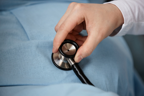 In the image a person is holding a stethoscope over a pregnant woman's belly listening to the baby's heartbeat.