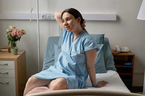 In this image a woman is sitting on a bed in a hospital room.