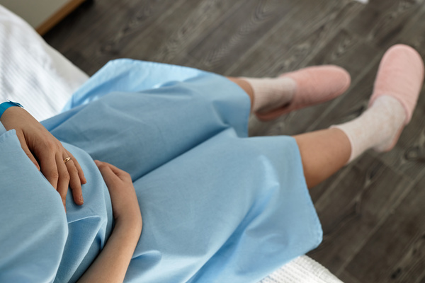 In this image a pregnant woman is lying down on a bed wearing a blue hospital gown.