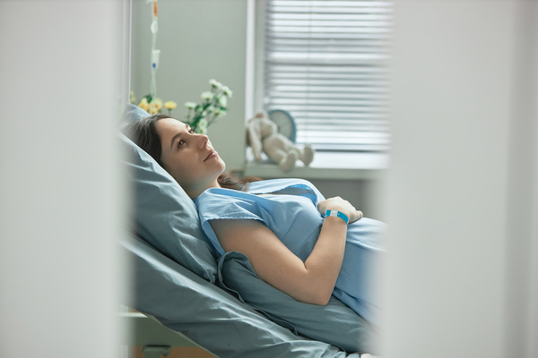 In this image a pregnant woman is lying down in a hospital bed wearing a blue hospital gown.