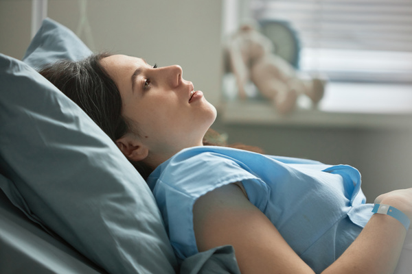 In this image a young woman is lying in a hospital bed wearing a blue hospital gown.