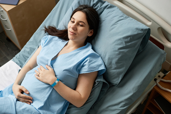 In this image a pregnant woman is lying down in a hospital bed.