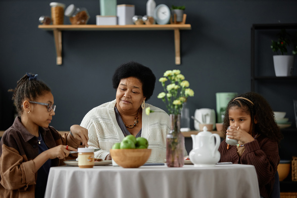 An Elderly Woman Sitting at a Table with Two Young Girls Eating