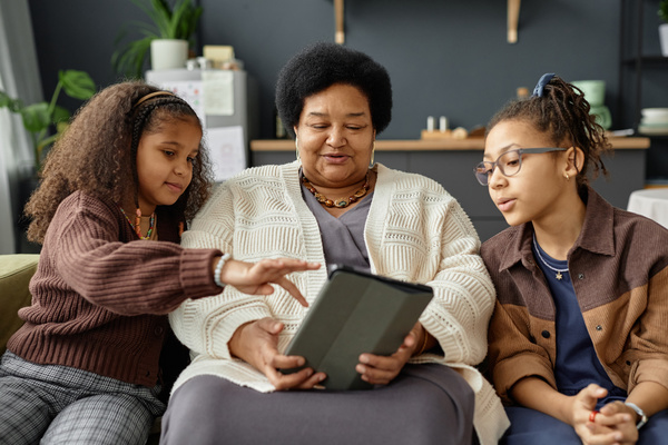 An Elderly Woman and Two Young Girls Looking at a Tablet Together