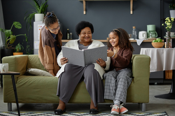 An Older Woman Sitting on a Couch with Two Young Girls Looking at a Book