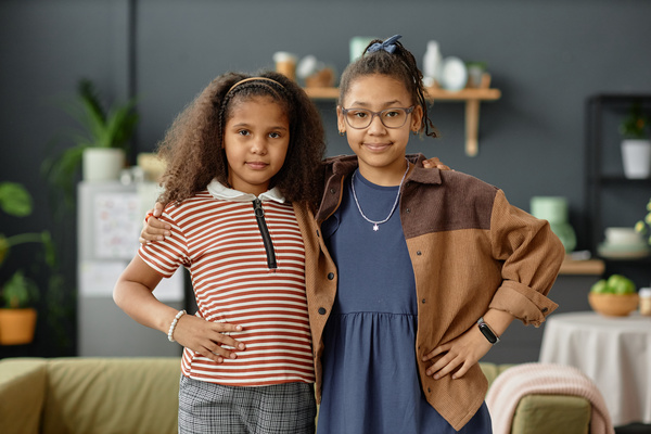 Two Young Girls Standing Next to Each Other in Front of a Couch