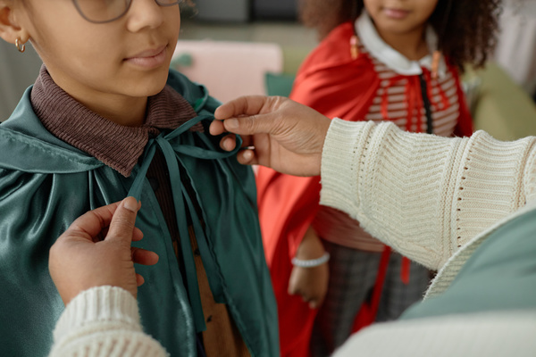A Woman Helping a Child Put on a Cape and Tie a Bow