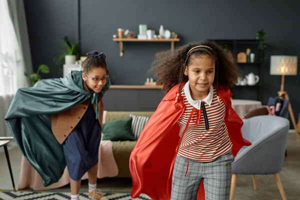 Two Young Girls Dressed As Superheroes in the Living Room of a House