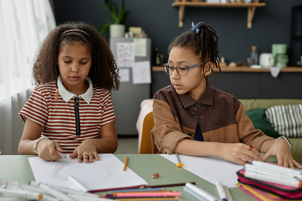 Two Young Girls Sitting at a Table with Paper and Colored Pencils