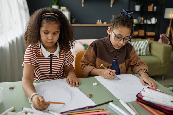 In this image two young girls are sitting at a dining table engrossed in drawing.
