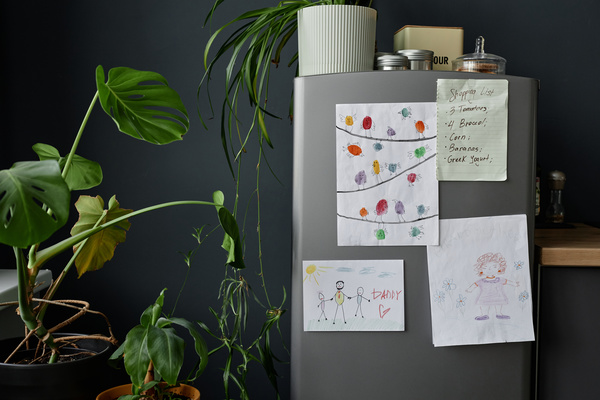 In this image a gray refrigerator is adorned with various pieces of artwork including children's drawings.